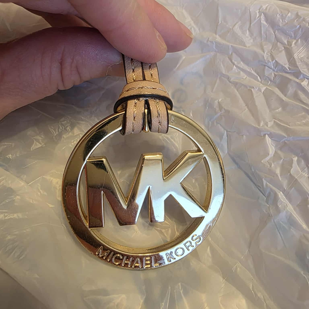 Michael Kors MK logo bag charm with a beige leather strap.
